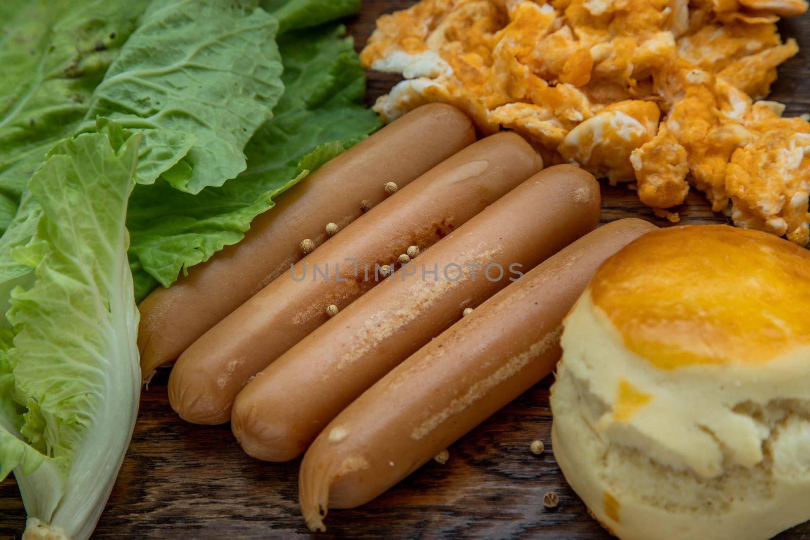 Close-up of fried sausages and scrambled eggs, scones with vegetable on wooden background. American breakfast, Selective focuse.