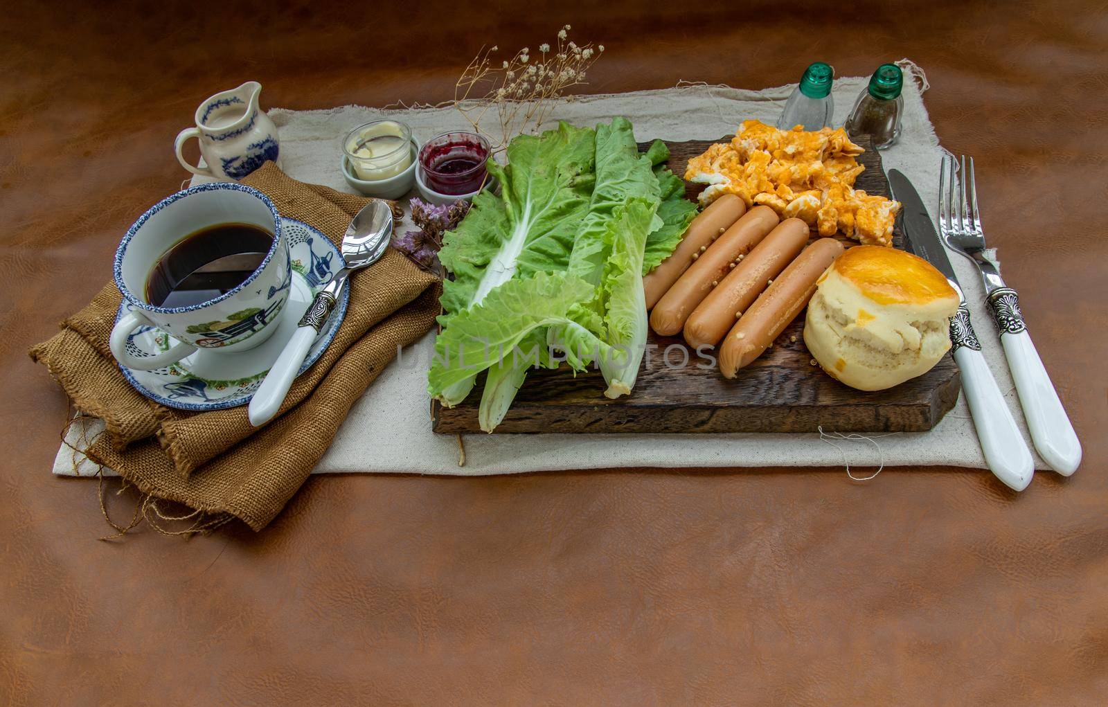 Continental breakfast with scrambled eggs, fried sausages, vegetable and scones served with coffee with milk. Wood background, Selective focuse.