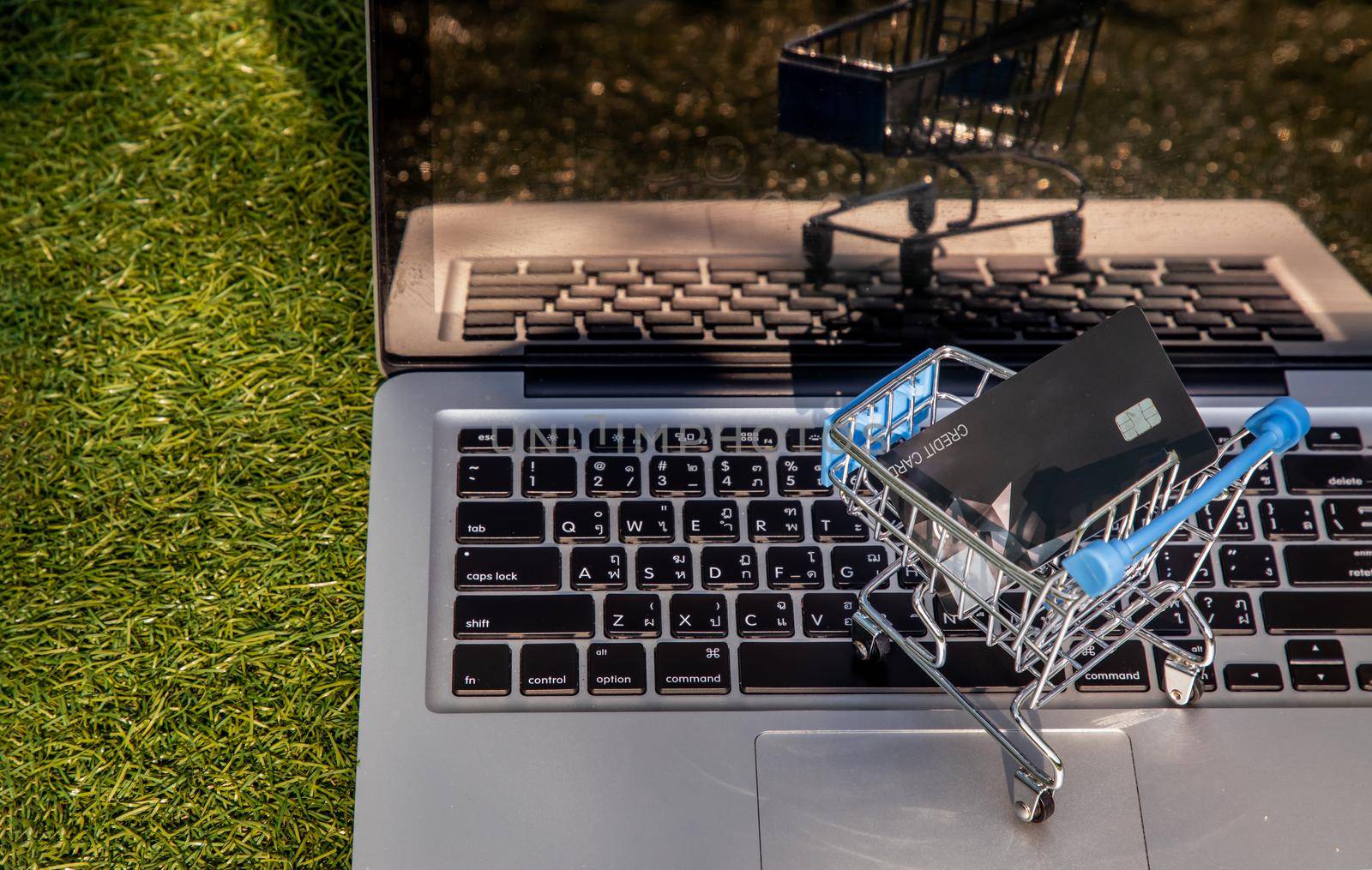 A credit card in a Mini supermarket trolley on a laptop keyboard. E-commerce and online shopping concept. Ideas about home shopping or buying things in virtual malls / stores from home or office by using modern technology called internet and web browser.