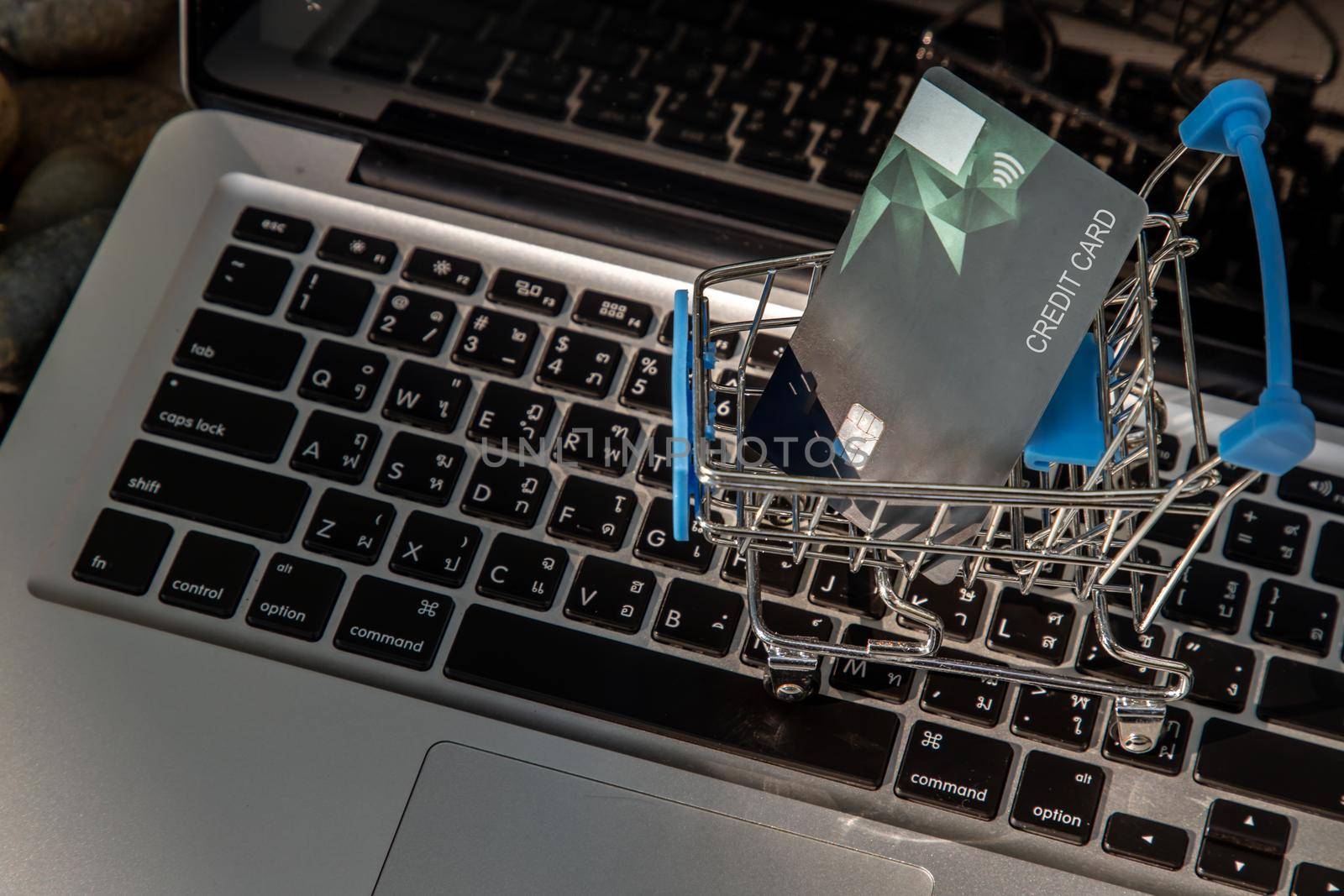 A credit card in a Mini supermarket trolley on a laptop keyboard. E-commerce and online shopping concept. Ideas about home shopping or buying things in virtual malls / stores from home or office by using modern technology called internet and web browser.