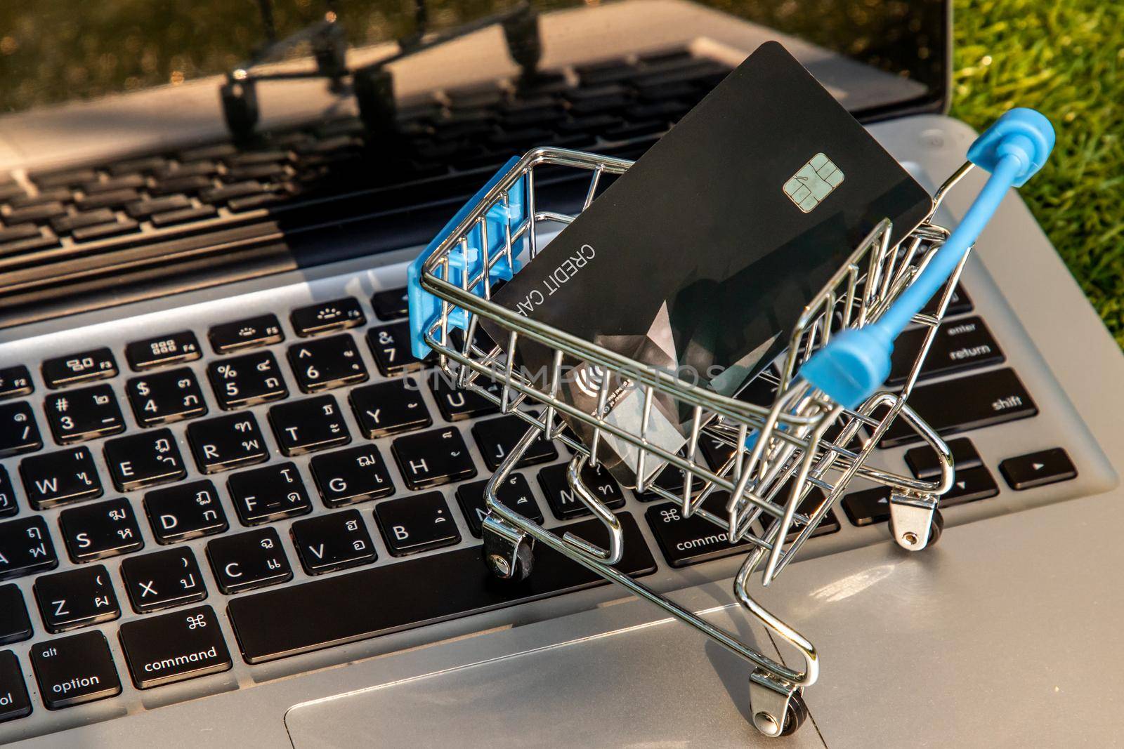 A credit card in a Mini supermarket trolley on a laptop keyboard. E-commerce and online shopping concept. Ideas about home shopping or buying things in virtual malls / stores from home or office by using modern technology called internet and web browser.