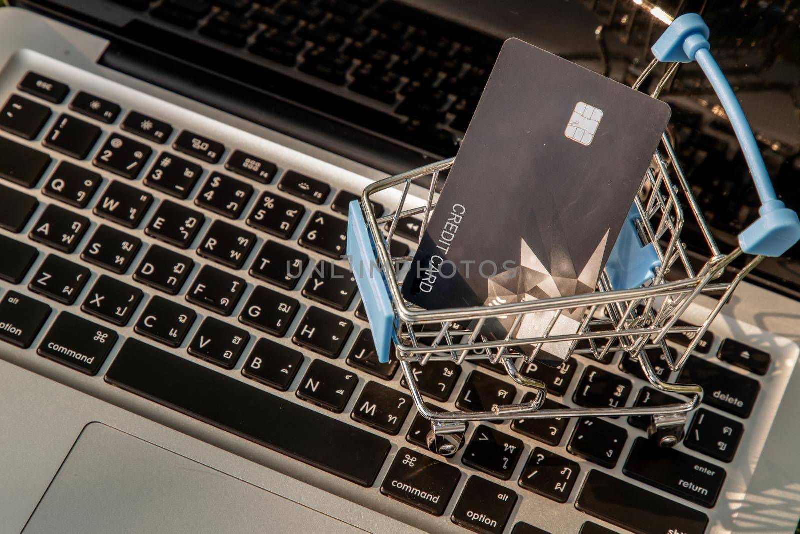 A credit card in a Mini supermarket trolley on a laptop keyboard. E-commerce and online shopping concept. Ideas about home shopping or buying things in virtual malls / stores from home or office by using modern technology called internet and web browser.