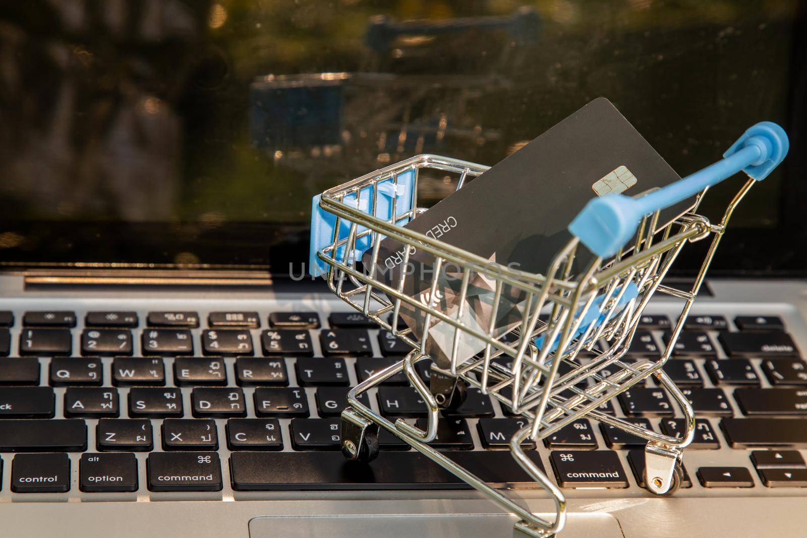 A credit card in a Mini supermarket trolley on a laptop keyboard. E-commerce and online shopping concept. Ideas about home shopping or buying things in virtual malls / stores from home or office by using modern technology called internet and web browser.