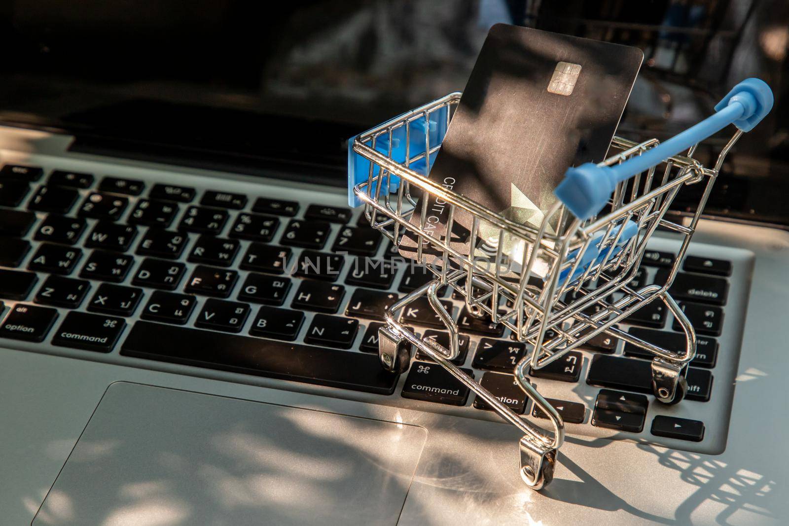 A credit card in a Mini supermarket trolley on a laptop keyboard. E-commerce and online shopping concept. Ideas about home shopping or buying things in virtual malls / stores from home or office by using modern technology called internet and web browser.