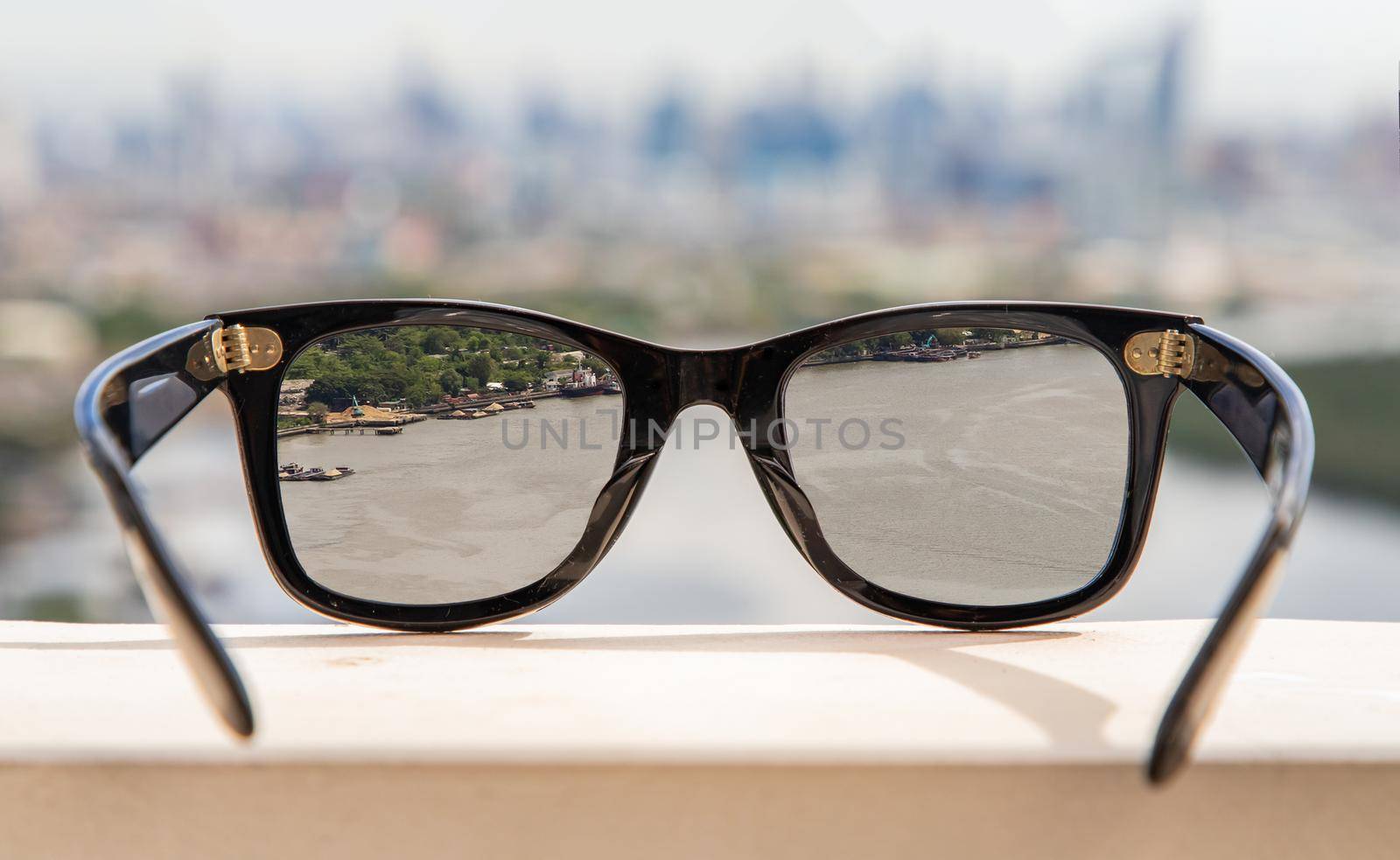 Bangkok, Thailand - Jun 09 2020 :  Black eyeglass on a reflective surface. View through the lens of glasses that look at the Chao Phraya River.