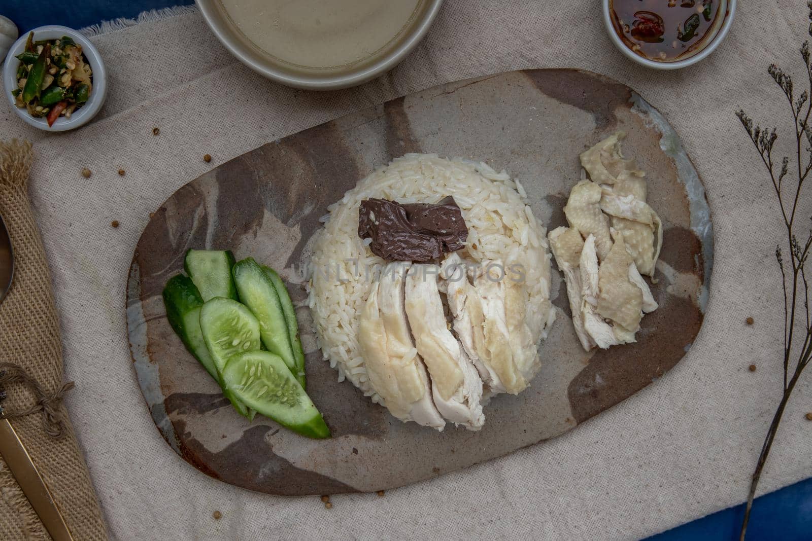 Hainanese chicken rice (Steam chicken with rice) with cucumber closeup on a plate and broth. Horizontal top view.