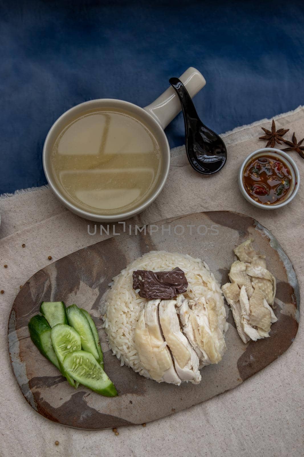 Hainanese chicken rice (Steam chicken with rice) with cucumber closeup on a plate and broth. Horizontal top view.