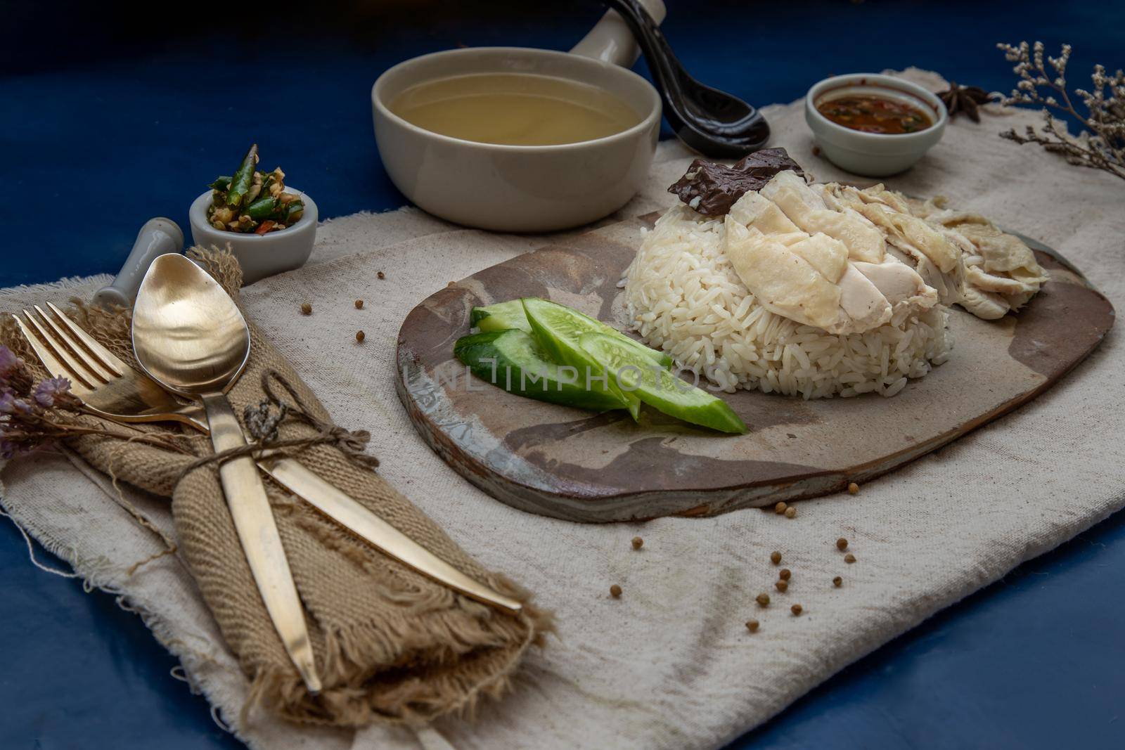 Hainanese chicken rice (Steam chicken with rice) with cucumber closeup on a plate and broth.