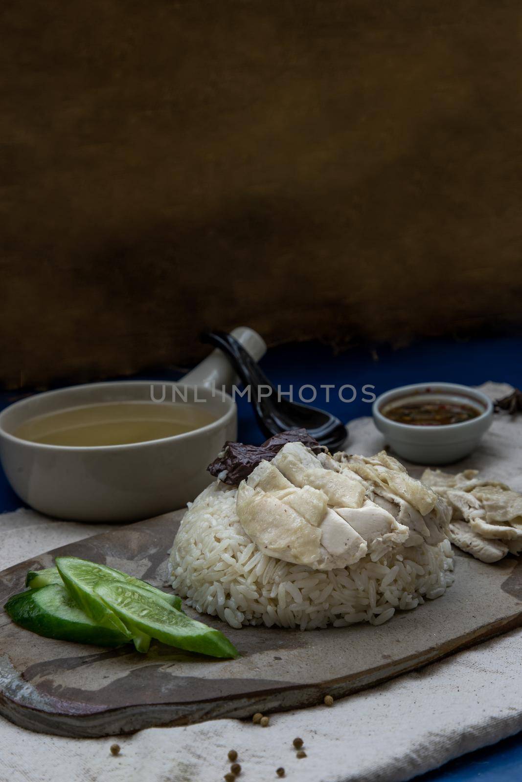 Hainanese chicken rice (Steam chicken with rice) with cucumber closeup on a plate and broth.