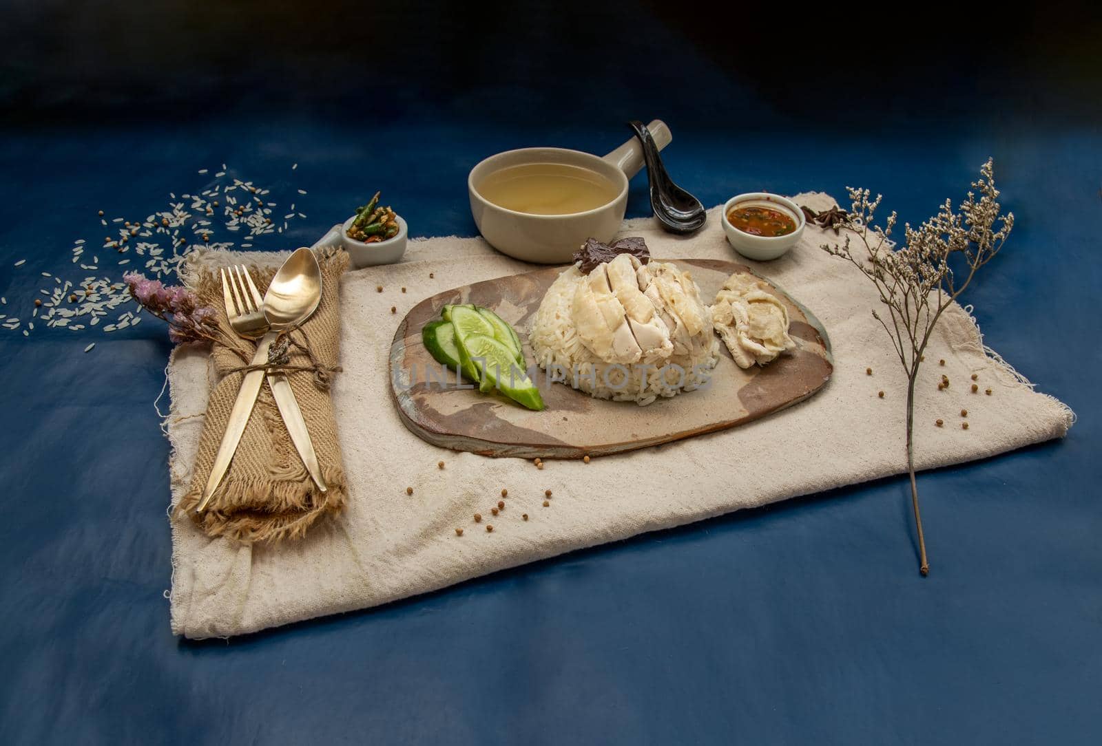 Hainanese chicken rice (Steam chicken with rice) with cucumber closeup on a plate and broth.