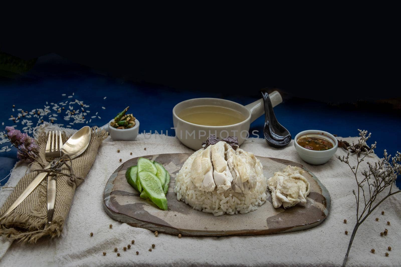 Hainanese chicken rice (Steam chicken with rice) with cucumber closeup on a plate and broth.
