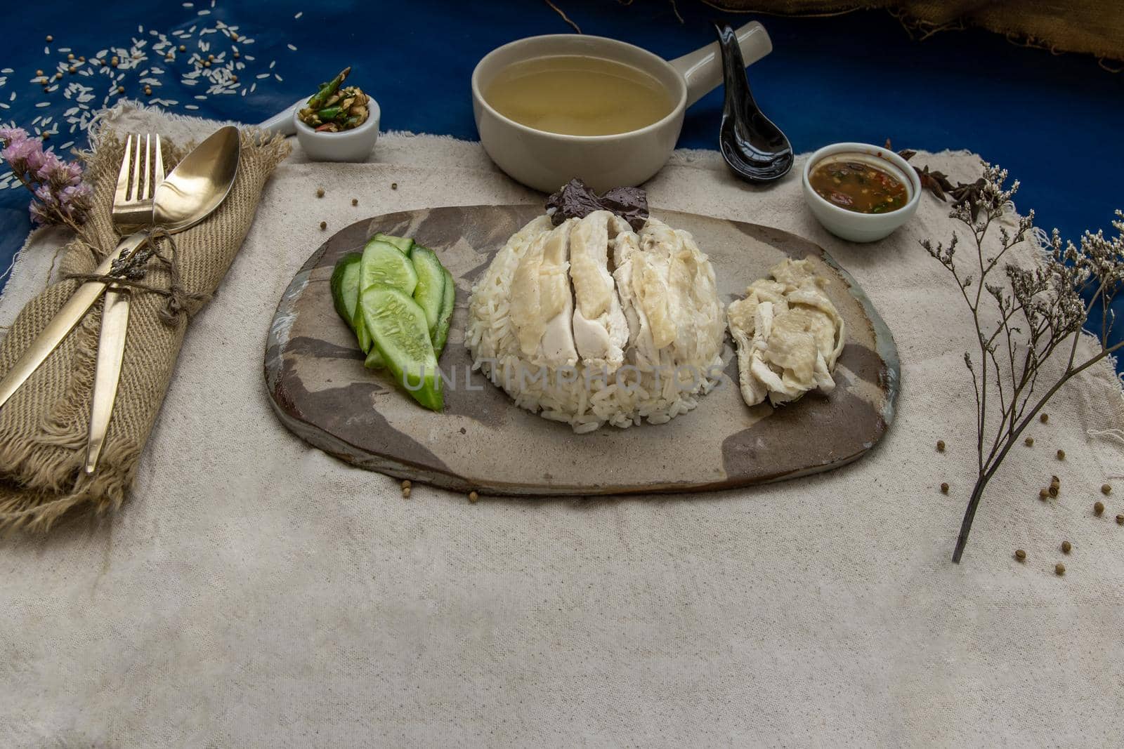 Hainanese chicken rice (Steam chicken with rice) with cucumber closeup on a plate and broth.
