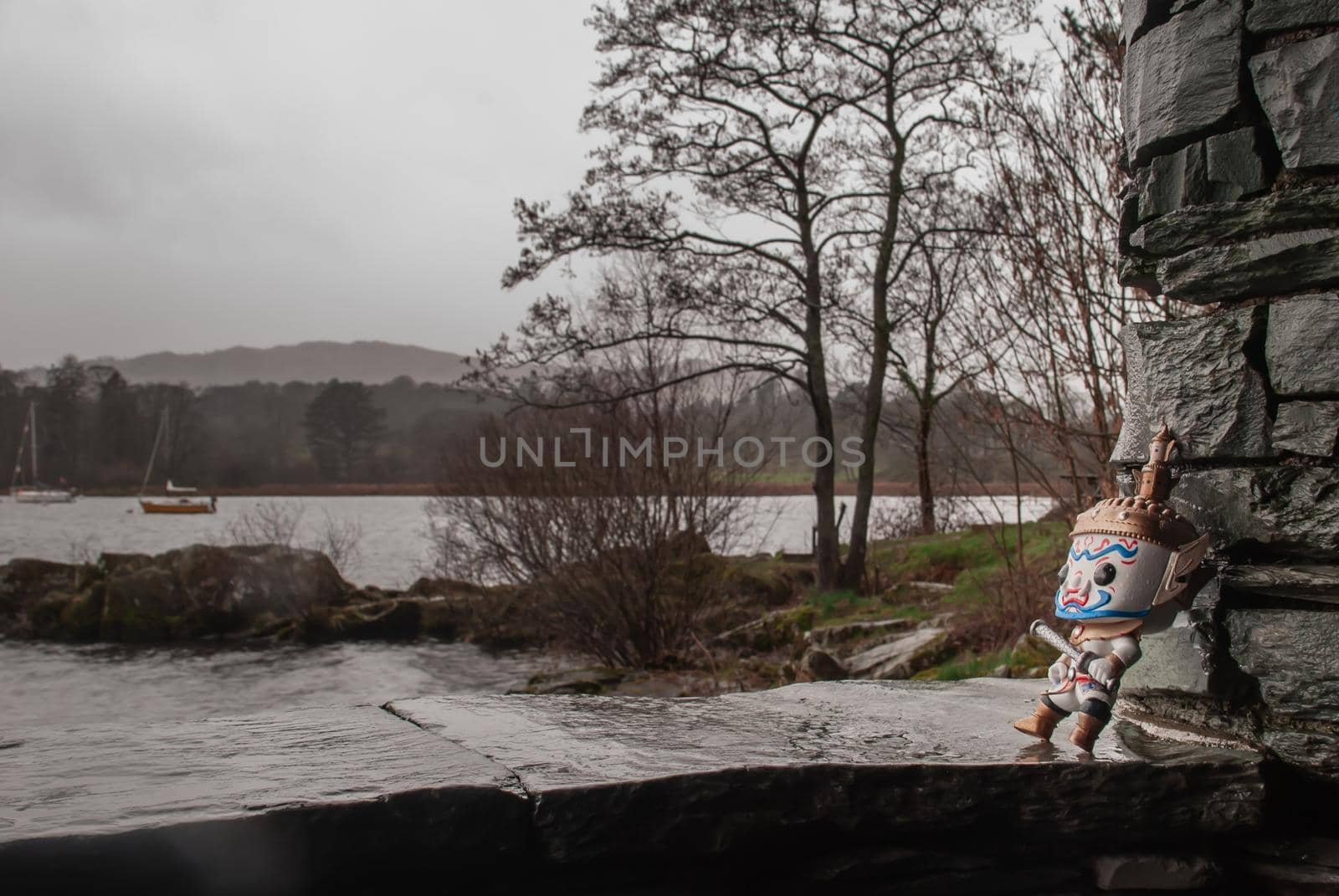 Ravana stood against a stone wall looking at the lake on a rainy day. Traveller doll.