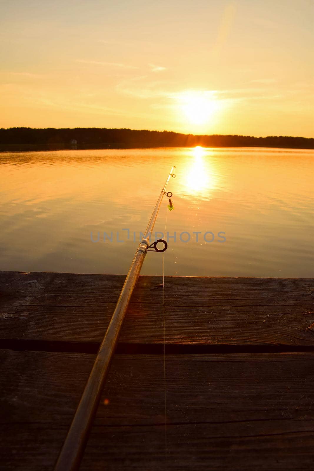 Close up high angle view of fishing rod on wooden pier at sunset hour, personal perspective
