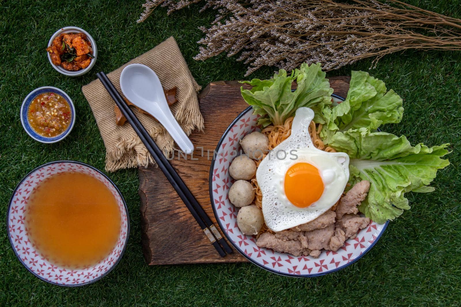 Boil egg noodles with pork ball, minced pork, fried egg, vegetables and soups in bowl and chopstick with spoon and timber background. Thai noodle soup.