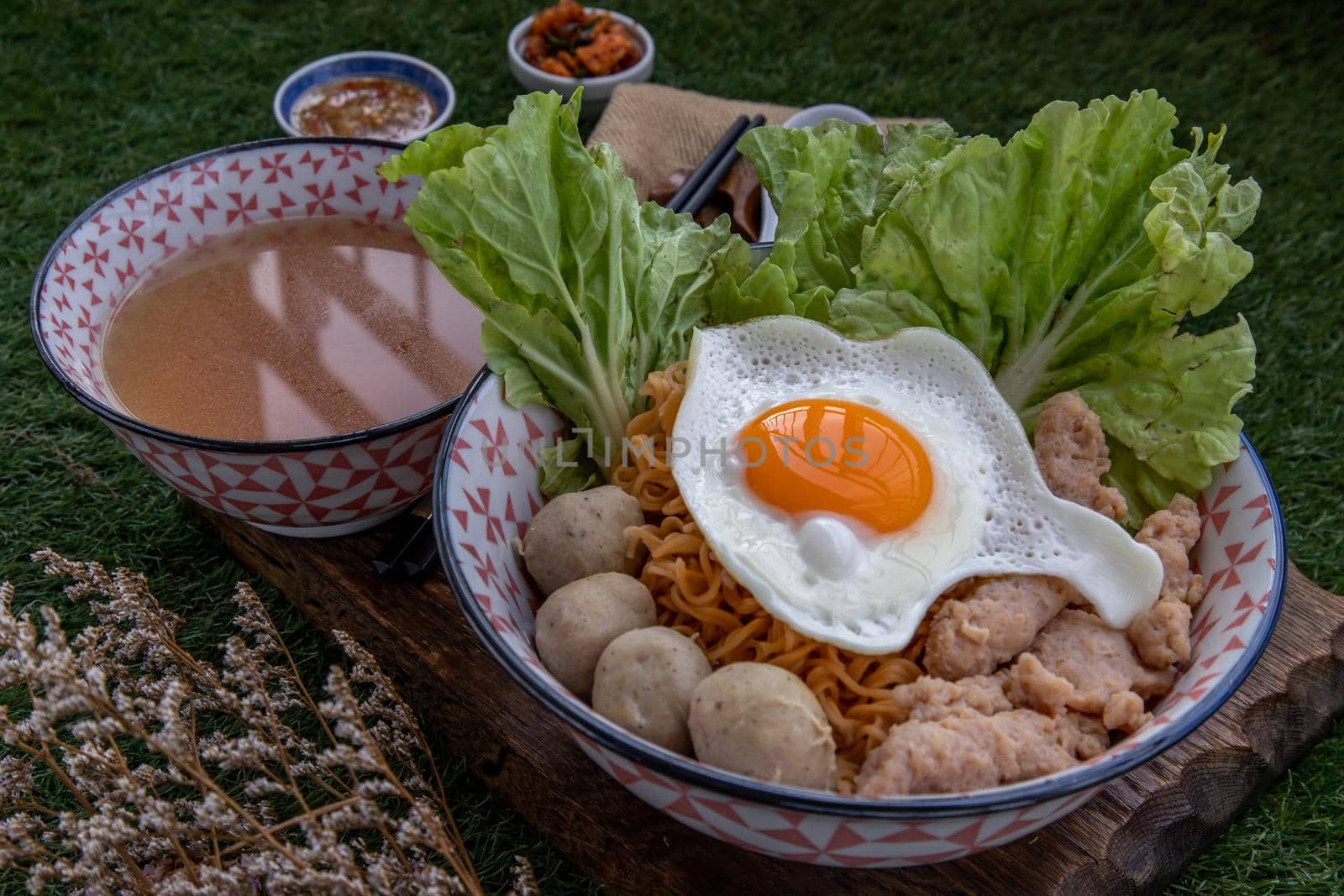 Boil egg noodles with pork ball, minced pork, fried egg, vegetables and soups in bowl and chopstick with spoon and timber background. Thai noodle soup.