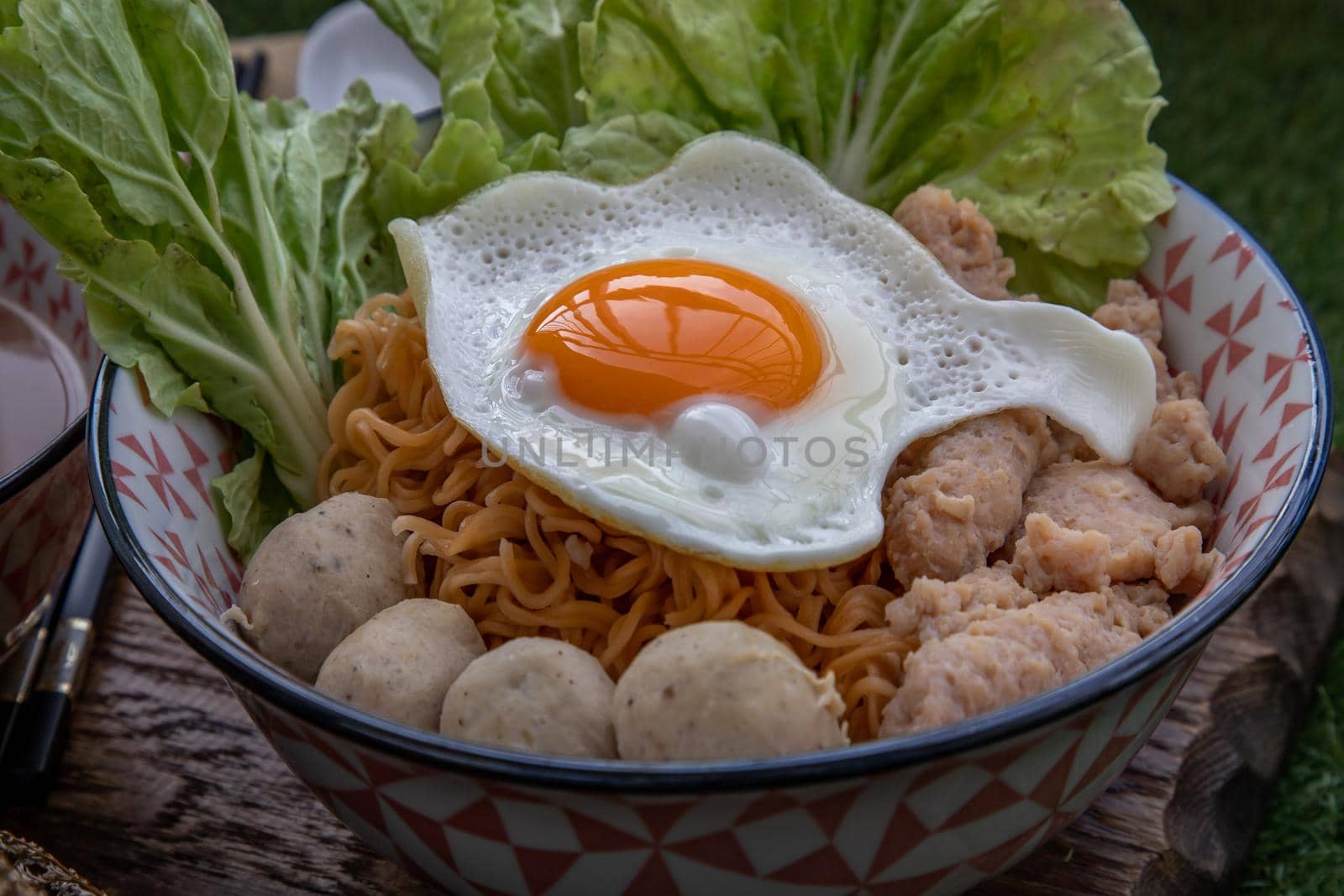 Boil egg noodles with pork ball, minced pork, fried egg, vegetables and soups in bowl and chopstick with spoon and timber background. Thai noodle soup.