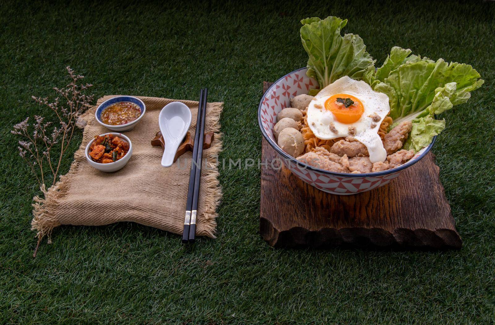 Egg noodles soup with pork ball, minced pork, fried egg, vegetables and soups in bowl and chopstick with spoon and timber background. Thai noodle soup.
