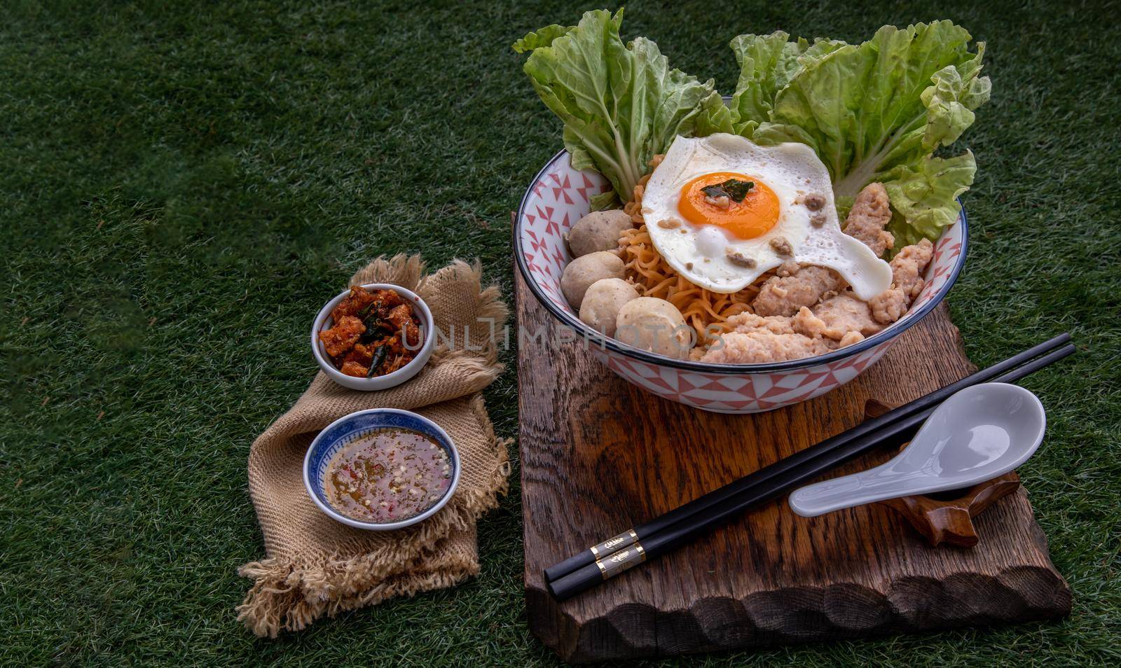 Egg noodles soup with pork ball, minced pork, fried egg, vegetables and soups in bowl and chopstick with spoon and timber background. Thai noodle soup.