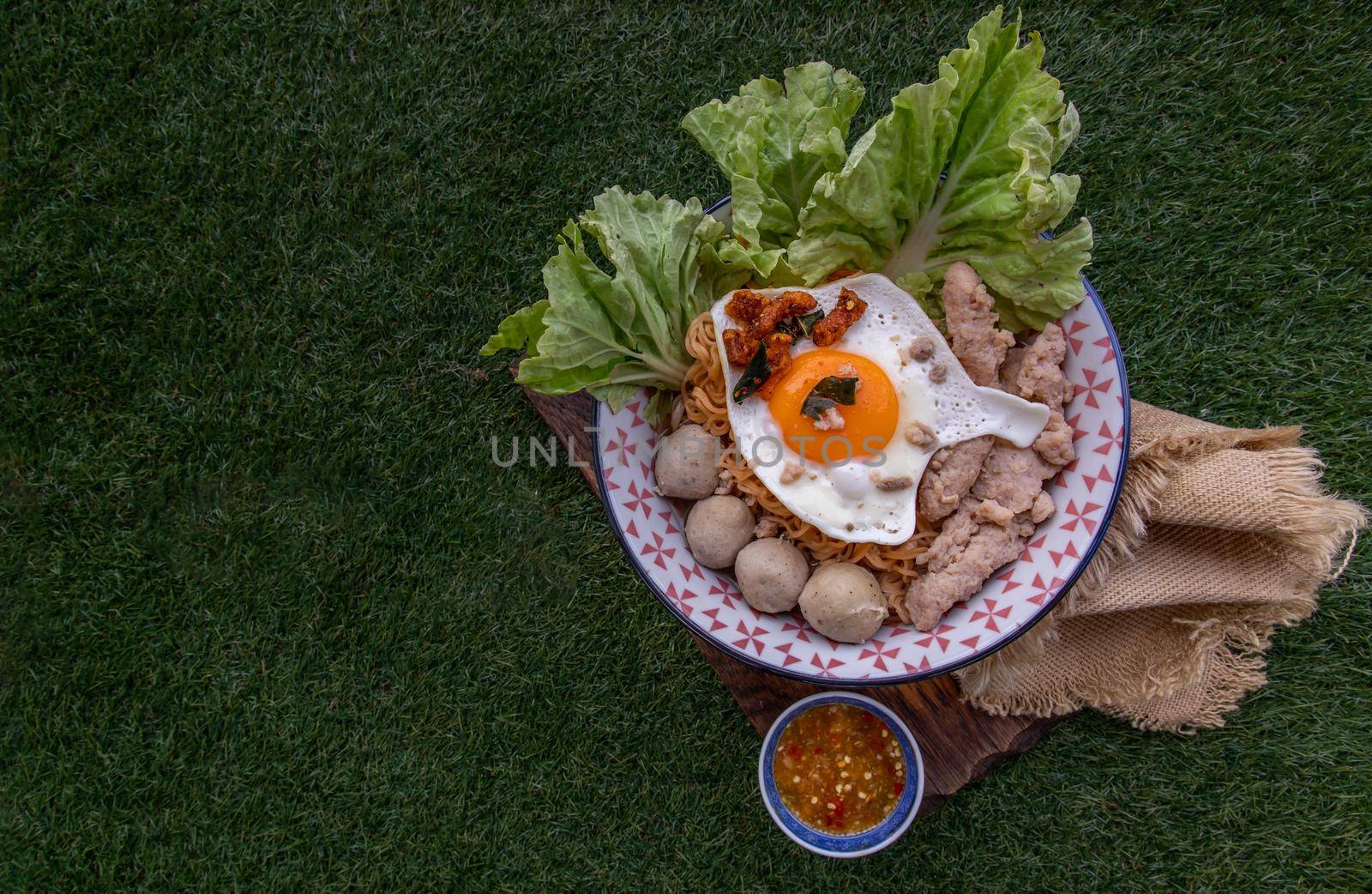 Egg noodles soup with pork ball, minced pork, fried egg, vegetables and soups in bowl and chopstick with spoon and timber background. Thai noodle soup.