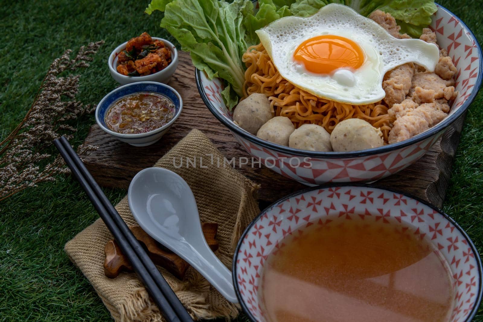 Boil egg noodles with pork ball, minced pork, fried egg, vegetables and soups in bowl and chopstick with spoon and timber background. Thai noodle soup.