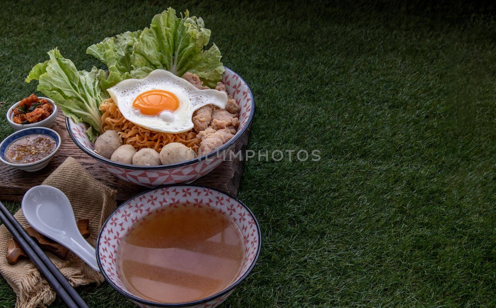 Boil egg noodles with pork ball, minced pork, fried egg, vegetables and soups in bowl and chopstick with spoon and timber background. Thai noodle soup.