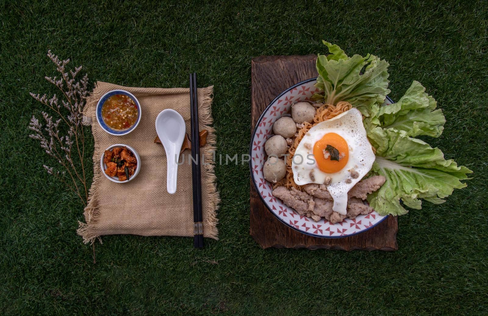 Egg noodles soup with pork ball, minced pork, fried egg, vegetables and soups in bowl and chopstick with spoon and timber background. Thai noodle soup.
