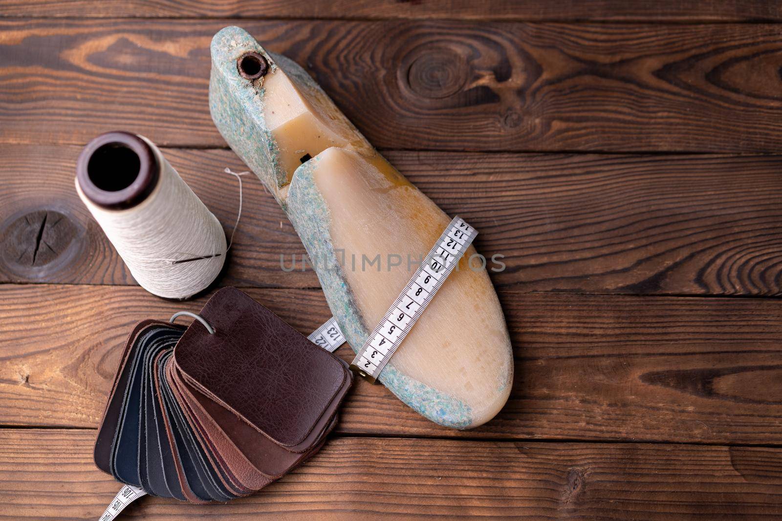 Leather samples for shoes and wooden shoe last on dark wooden table. Designer furniture clothes. Shoe maker workspace.