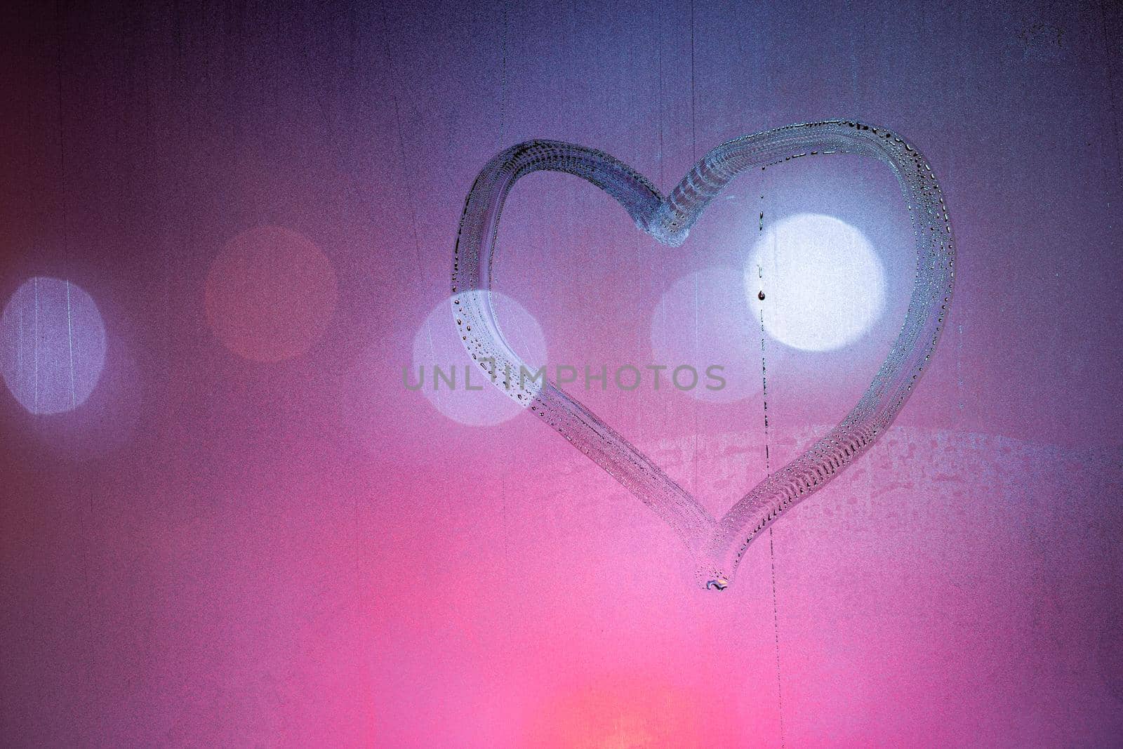 heart symbol hand drawn on wet night window glass in pink colors.