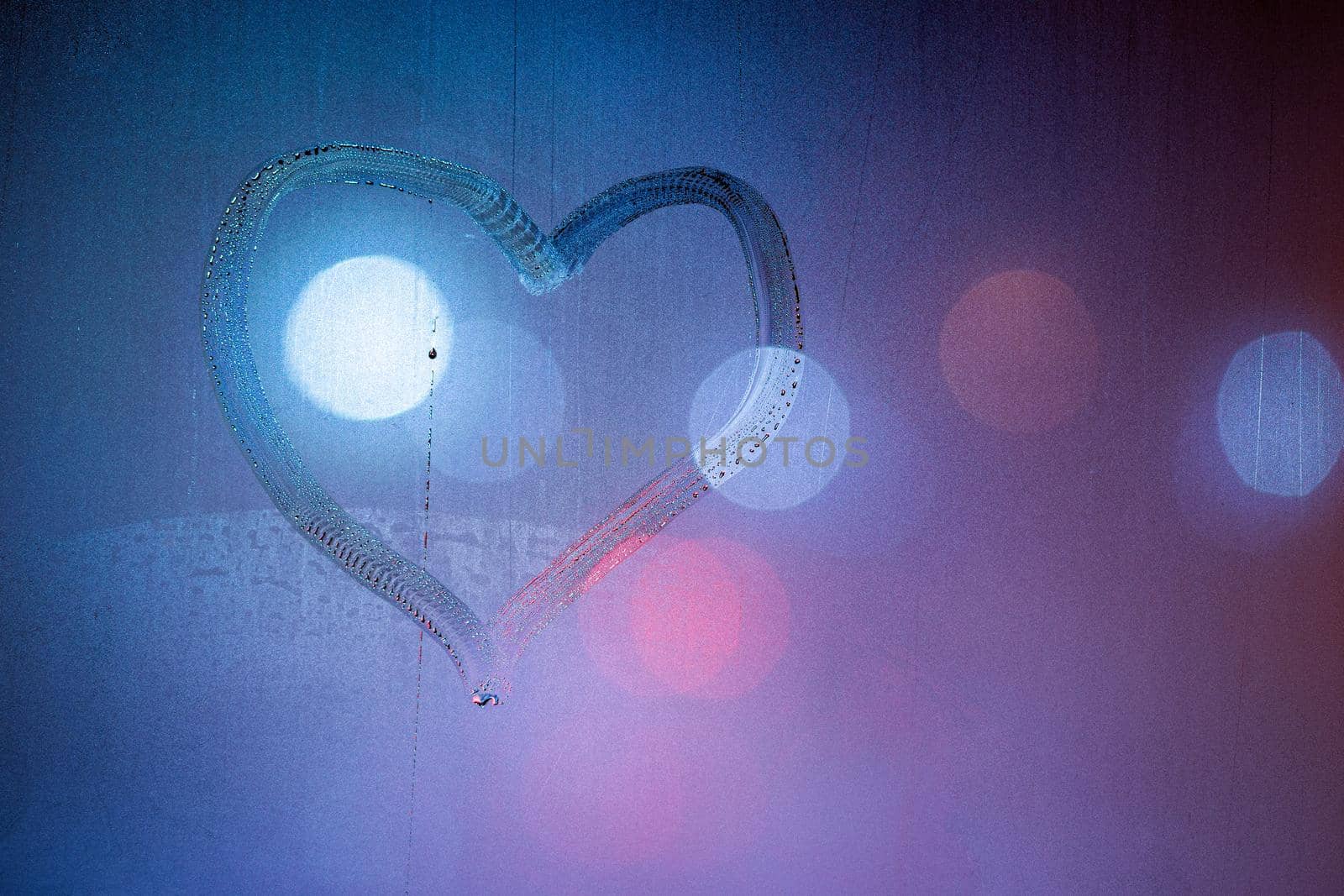 heart symbol hand drawn on wet night window glass in blue colors.