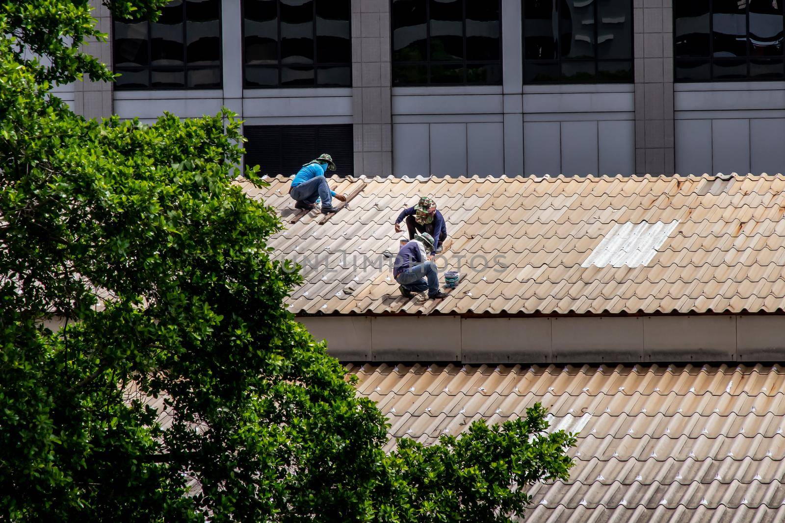 Bangkok, Thailand - 13 Jun 2020 : Three handyman workers repairing tiles on the damaged factory roof.