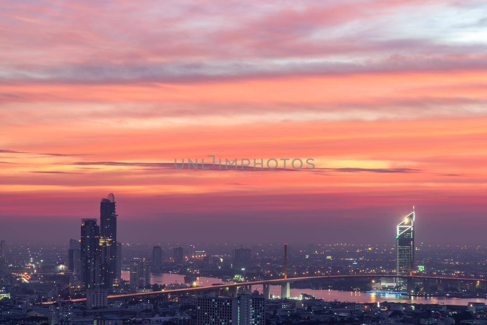 Bangkok, thailand - Dec 23, 2020 : Aerial view of Bangkok city Overlooking Skyscrapers and the Bridge crosses the Chao Phraya river with bright glowing lights at dusk. No focus, specifically.