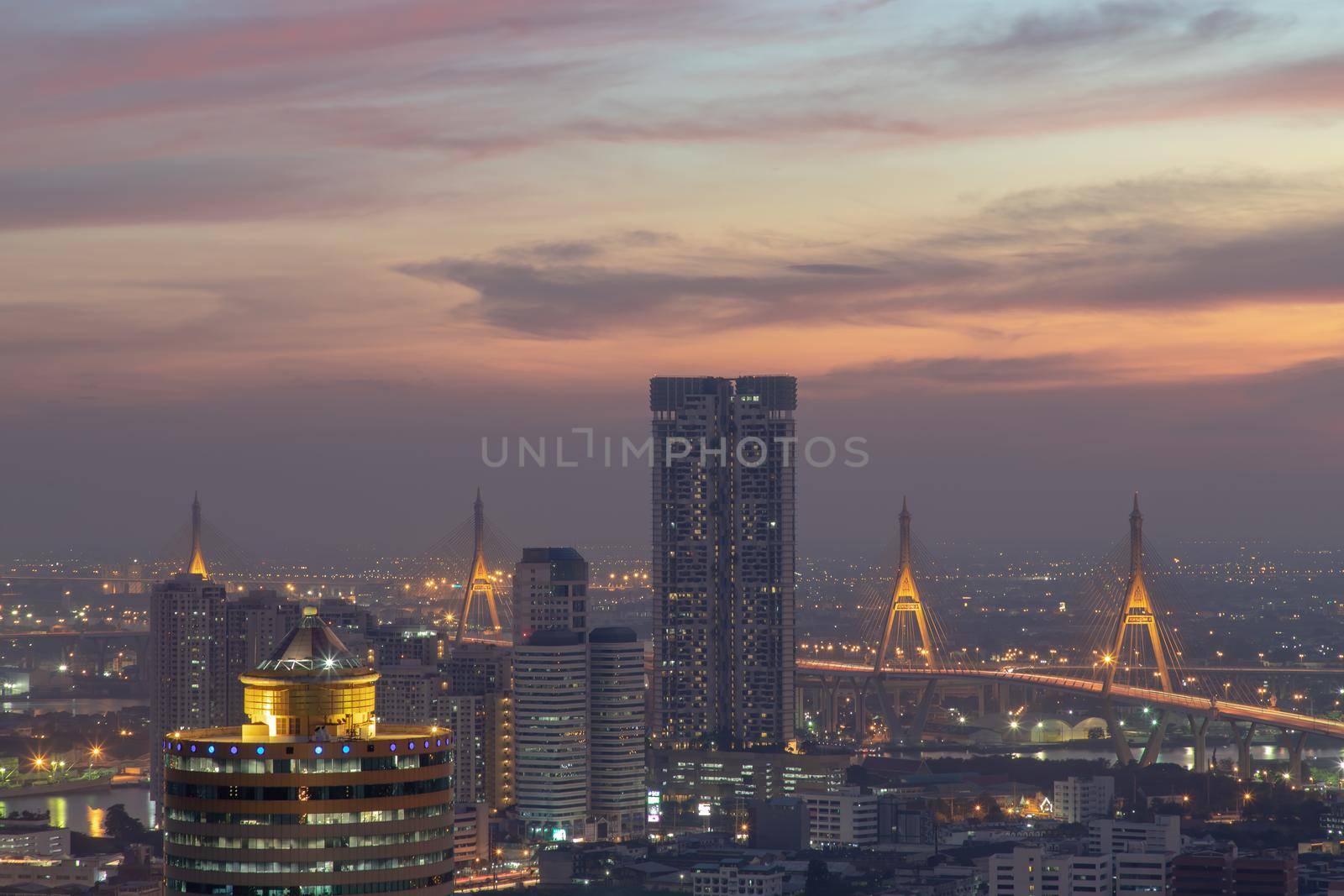 Bangkok, thailand - Dec 23, 2020 : Aerial view of Bangkok city Overlooking Skyscrapers and the Bridge crosses the Chao Phraya river with bright glowing lights at dusk. No focus, specifically.
