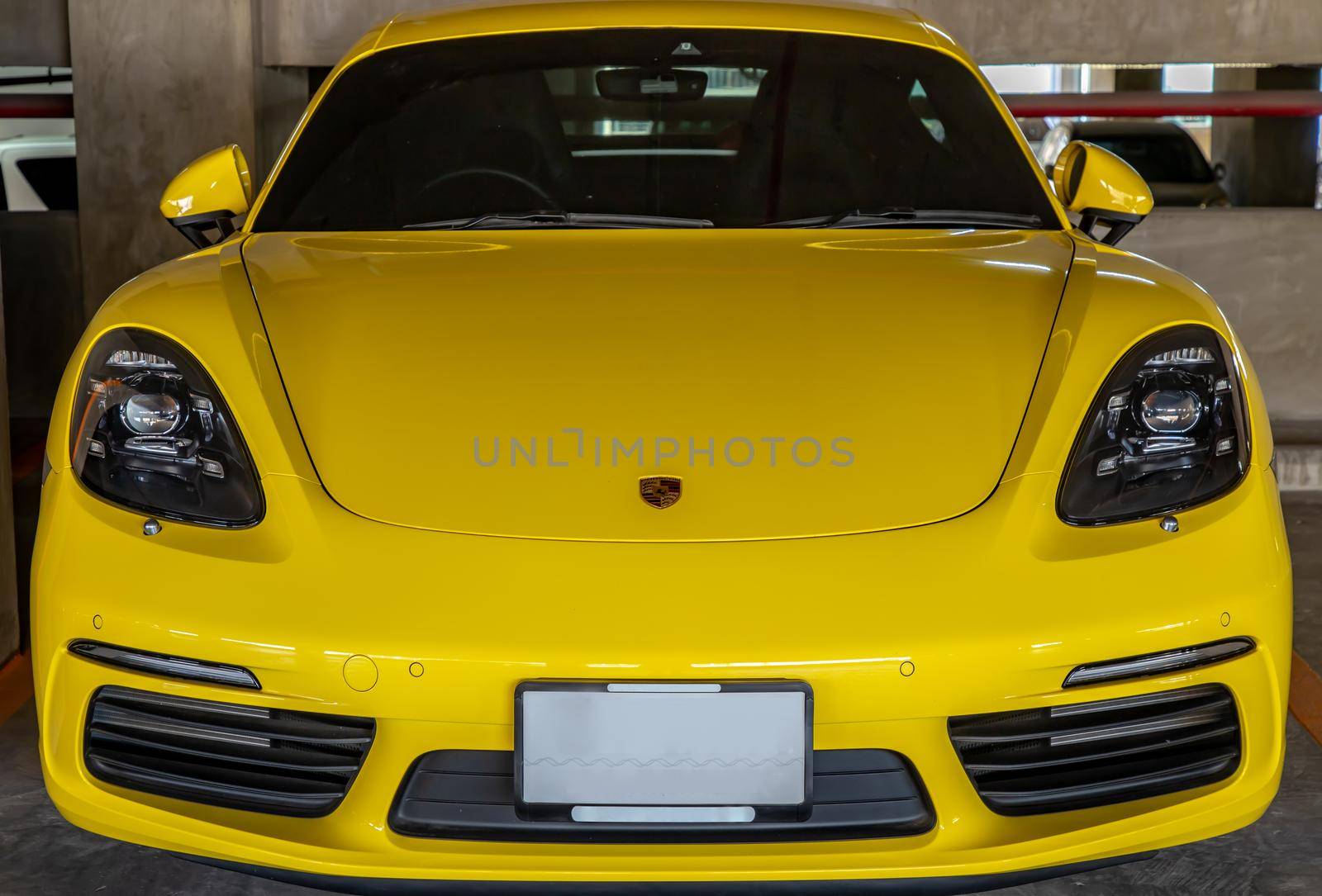 In front of yellow Porsche Sports Car parked in the parking lot.  by tosirikul