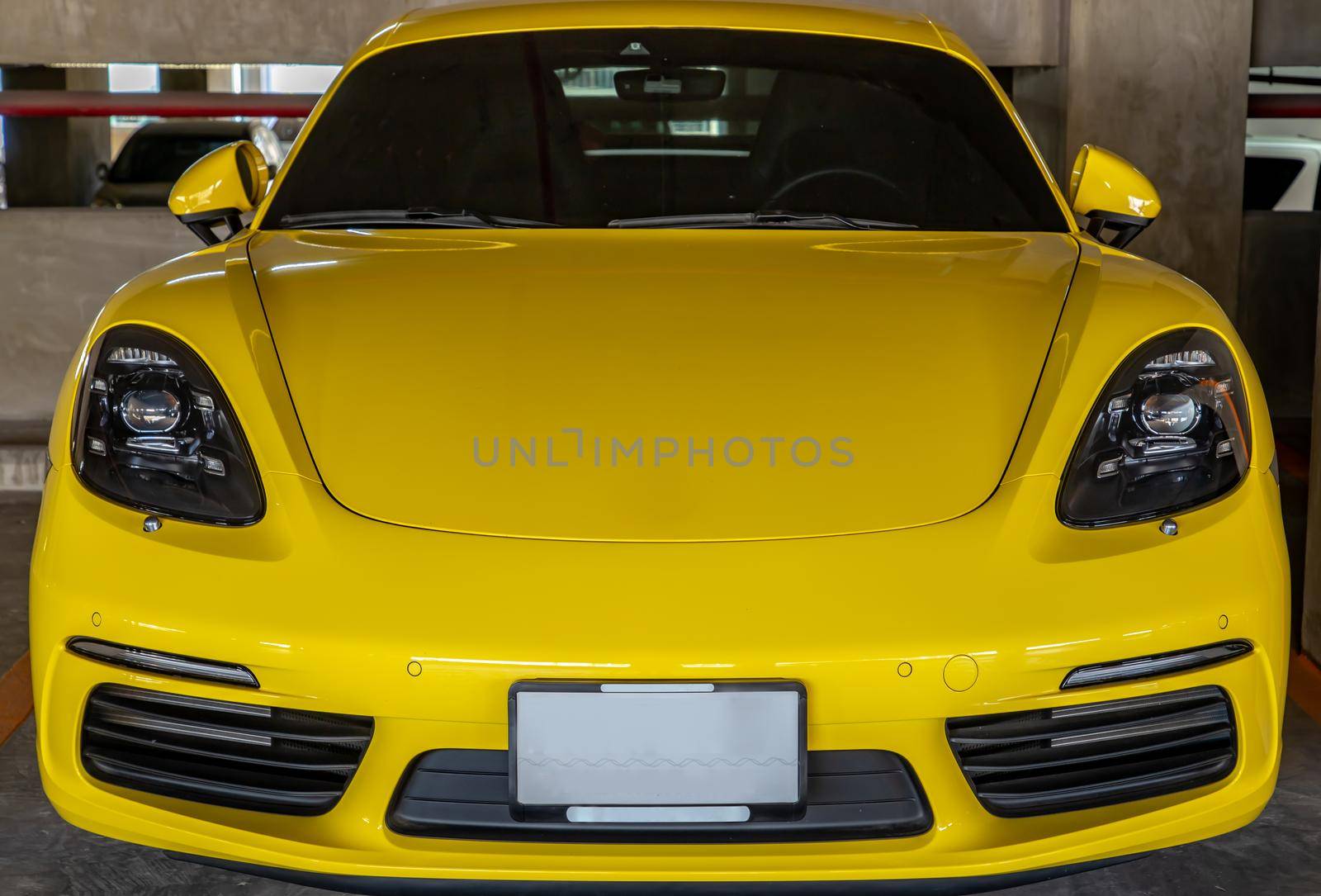 In front of yellow Porsche Sports Car parked in the parking lot.  by tosirikul