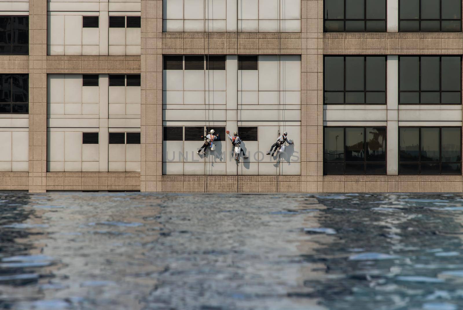Group of workers cleaning windows service on high rise office building with reflection from swimming pool. Selective focus.