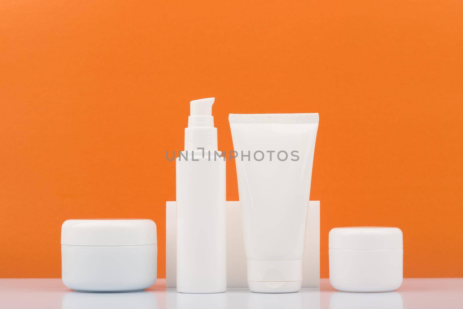 Set of cosmetic bottles on white glossy table against orange background. Beauty products with citrus extracts and oils by Senorina_Irina