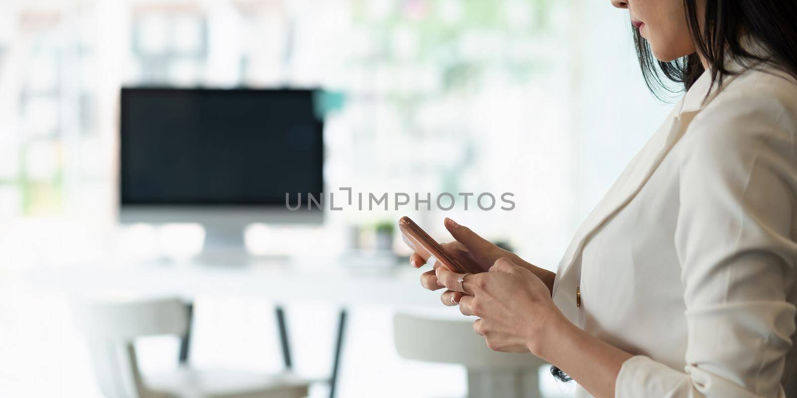 Businesswoman using smartphone at her office with workplace background.