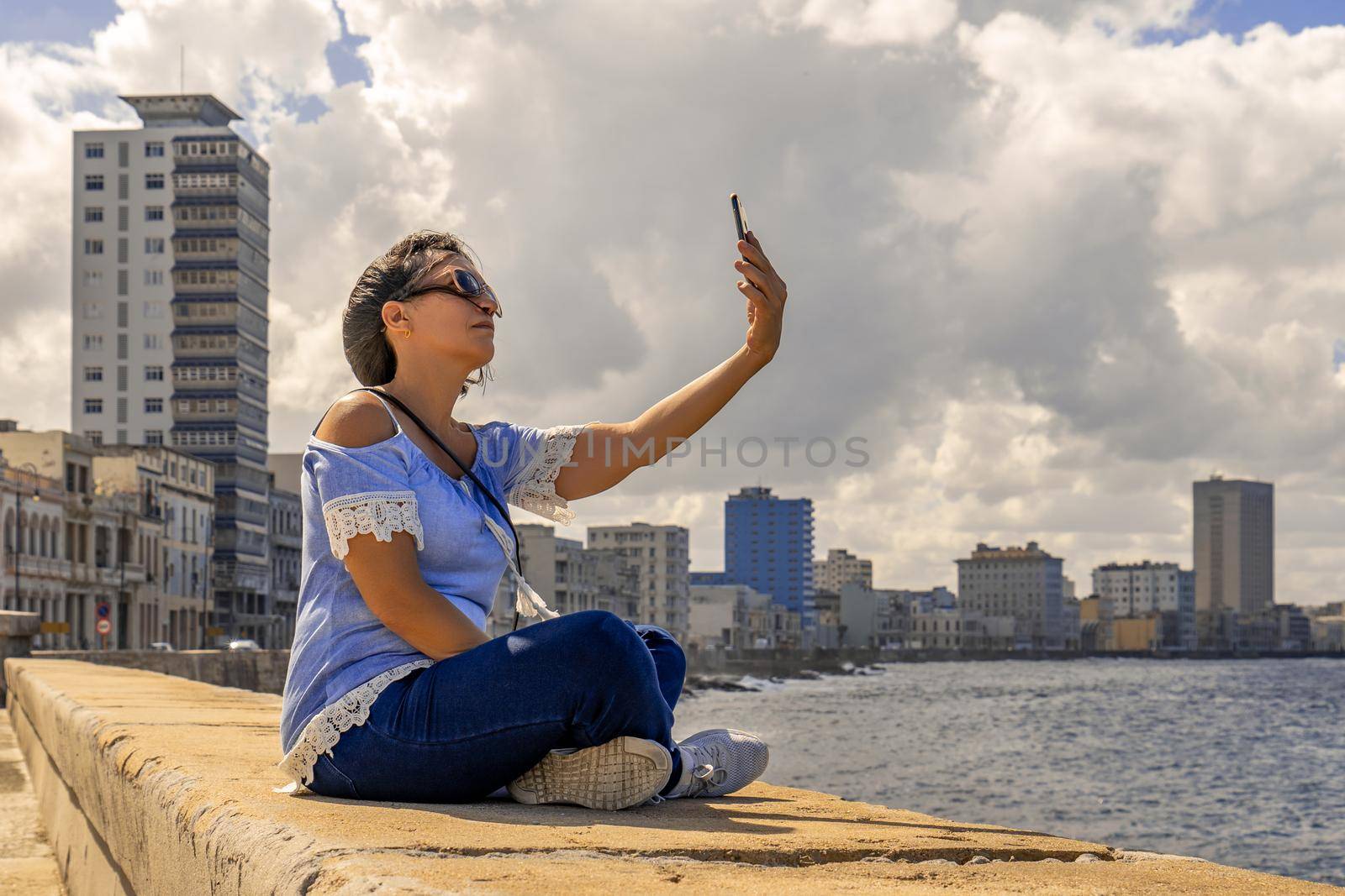 Woman sitting on the Malecon in Havana in front of the sea using a cell phone