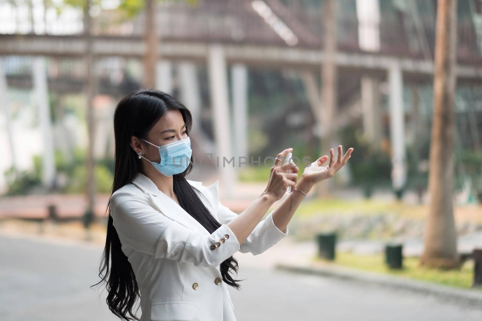 Portrait of businesswoman wearing mask sanitizing hands at post pandemic office, copy space. by nateemee