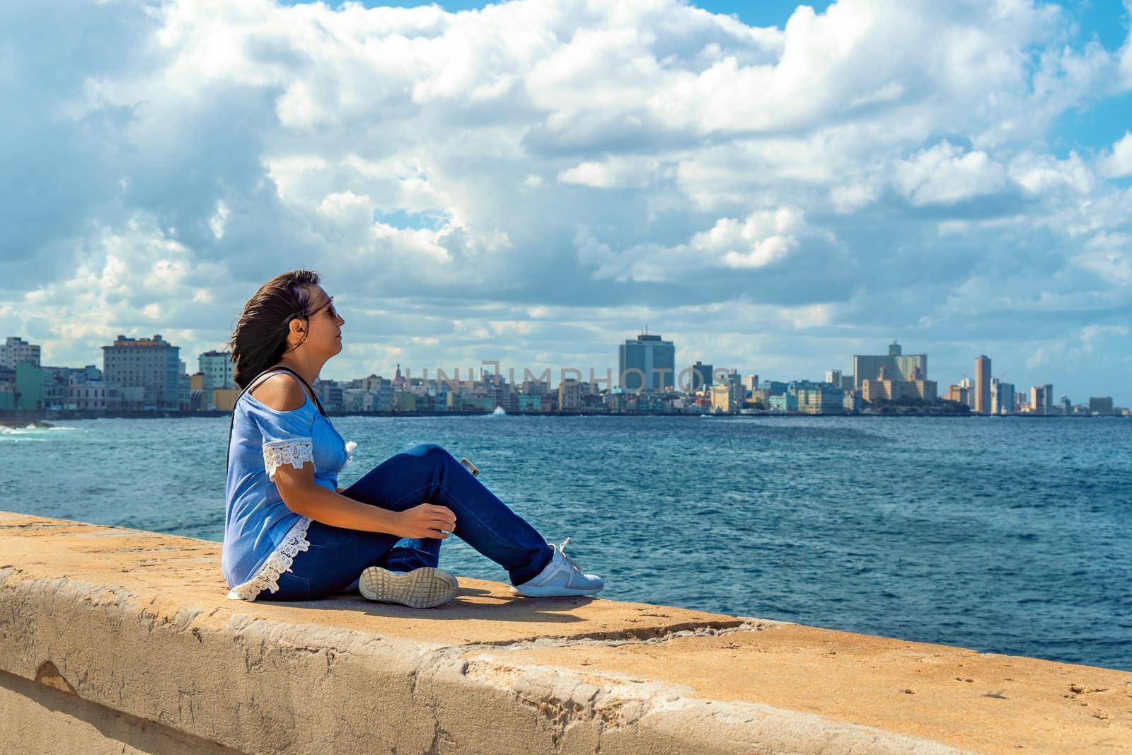 Woman sitting on the Malecon in Havana in front of the sea.