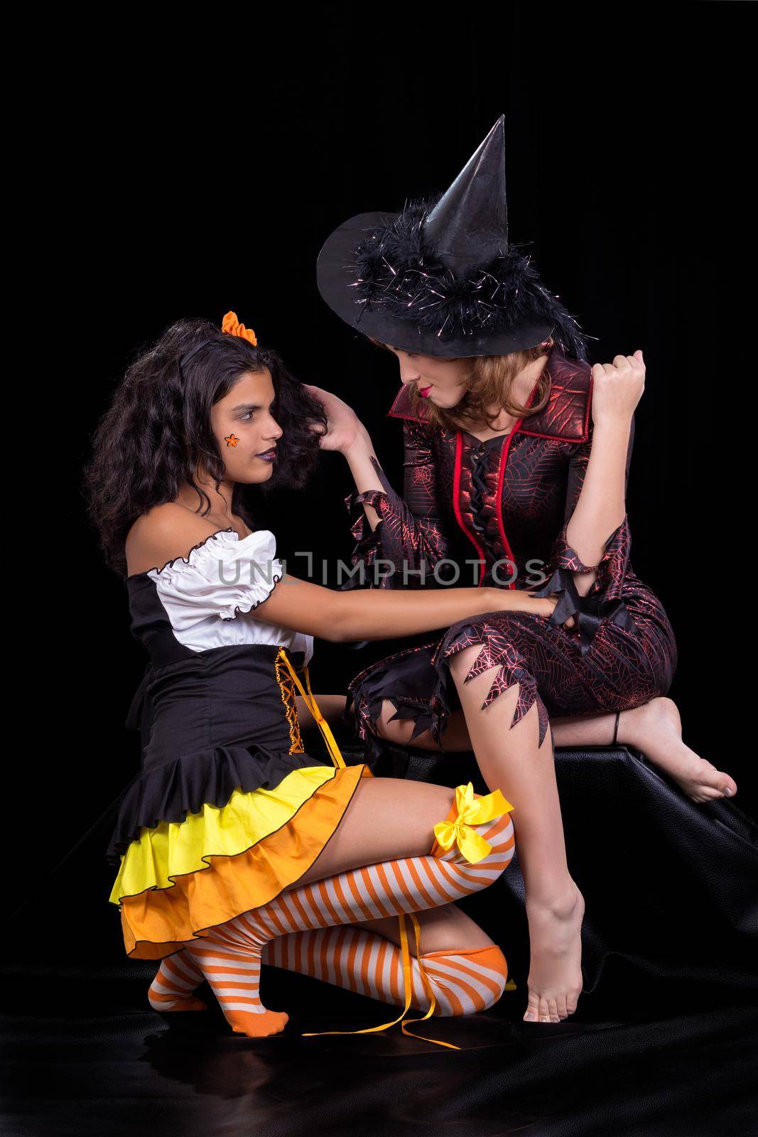 girl dressed as doll and another girl dressed as a witch both portrayed on black background