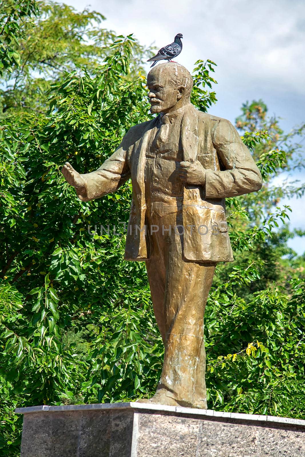 Statue of Soviet leader Lenin. There's a pigeon on his head. Sunny summer day. Side view. Crimea, Sudak - 10 October 2020. by Essffes