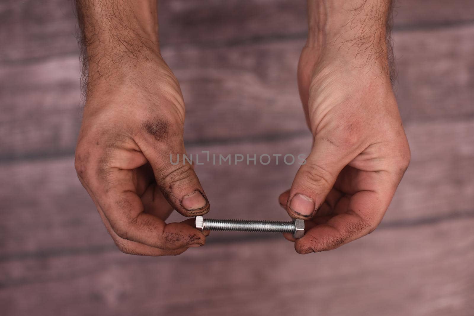 Men's hands tighten the nut on the bolt. The worker's hands are dirty. Close-up.