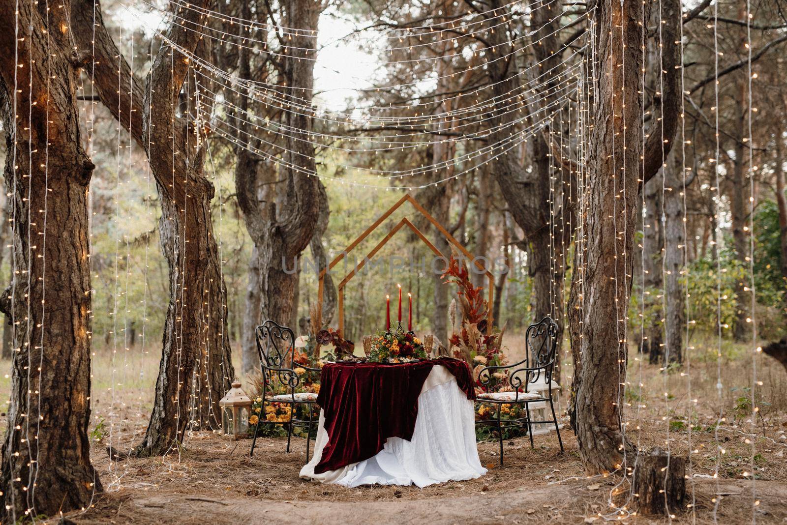 The wine presidium of the newlyweds in the banquet hall of the restaurant is decorated with candles and green plants, wisteria hangs from the ceiling