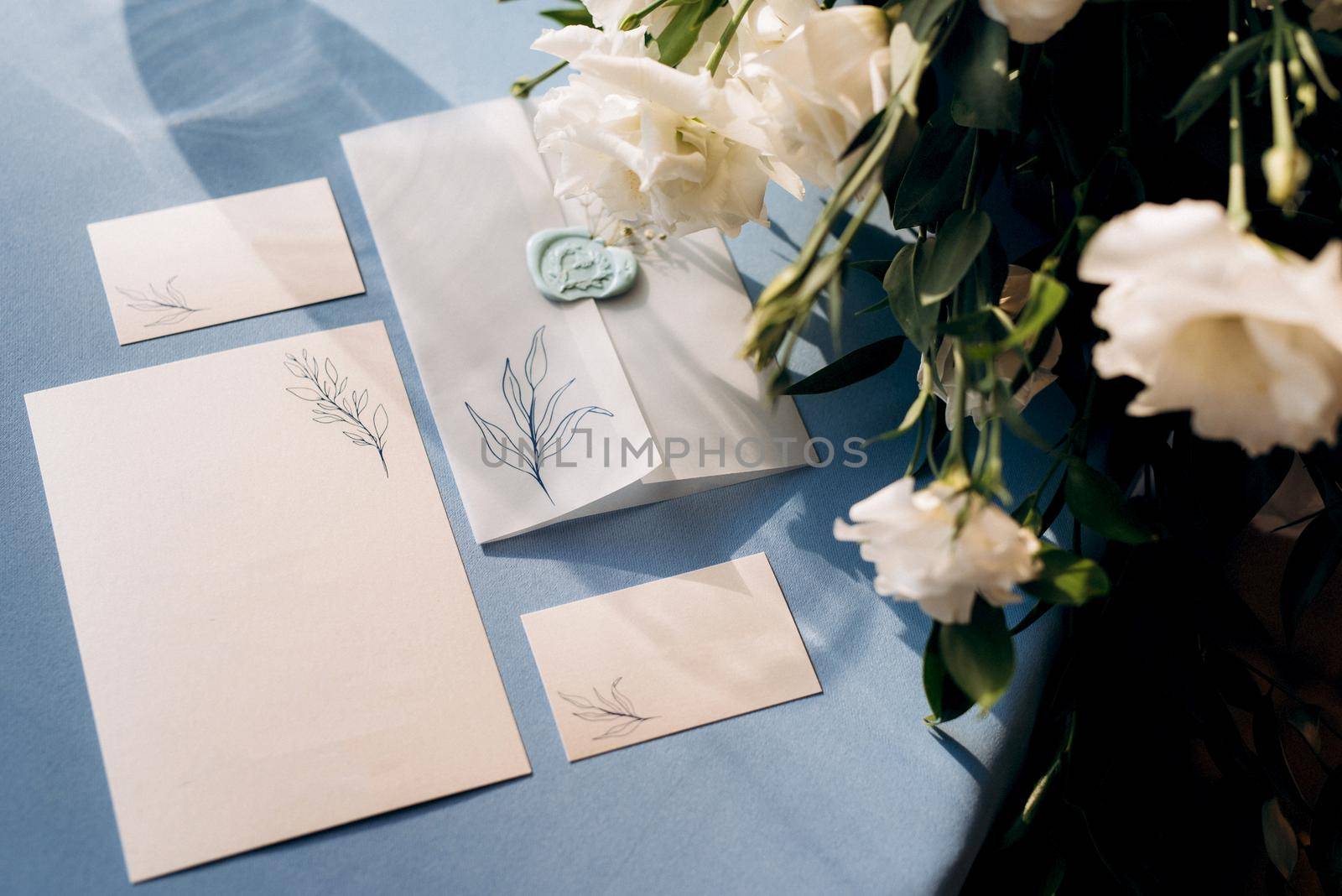 wedding invitation in a blue envelope on a table with green sprigs