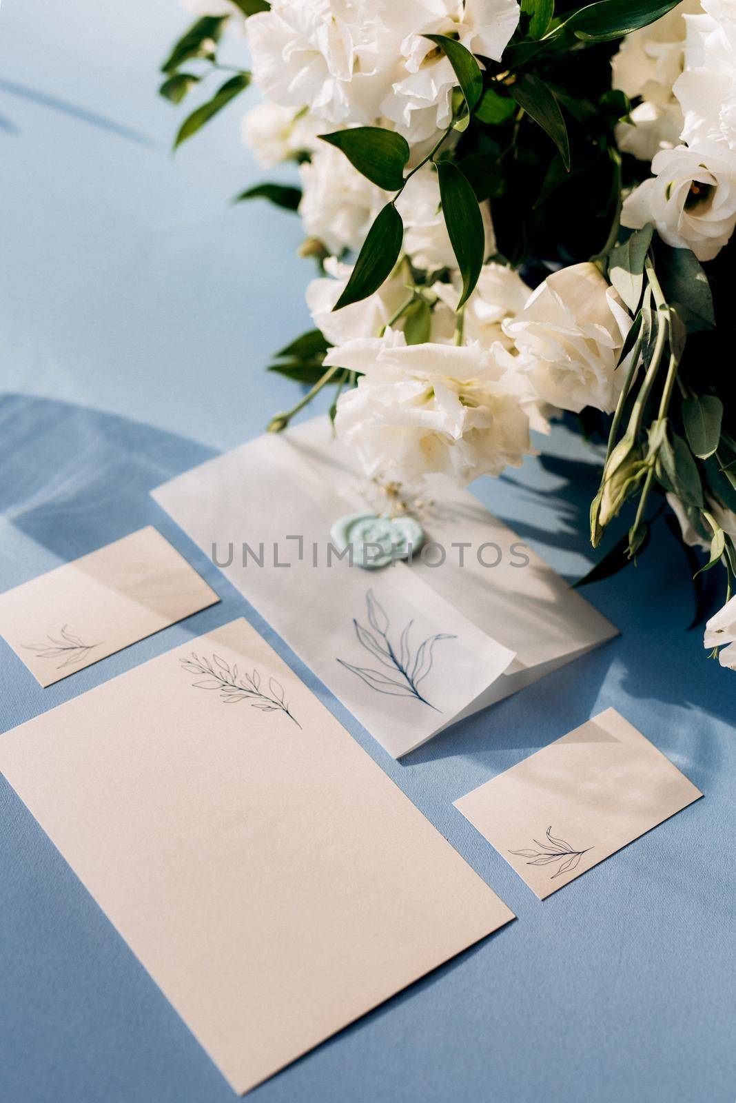 wedding invitation in a blue envelope on a table with green sprigs