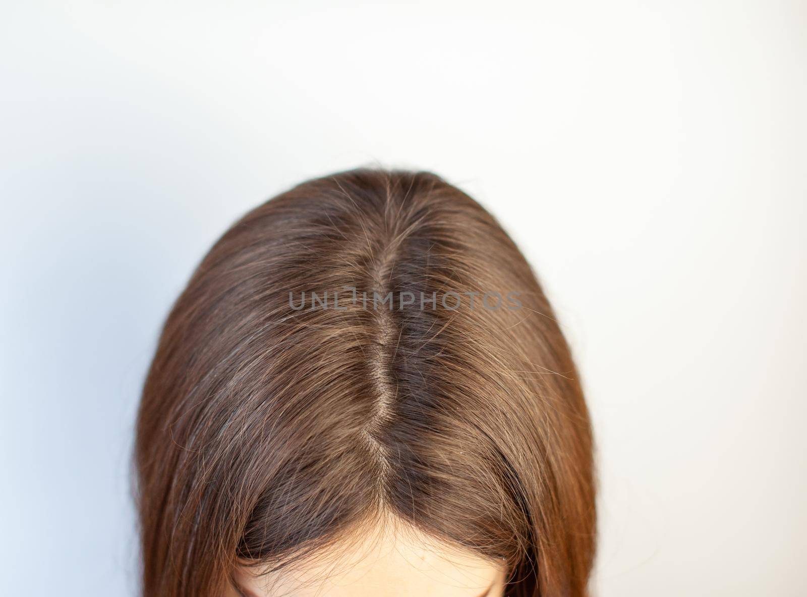 A woman's head with a parting of gray hair that has grown roots due to quarantine. Brown hair on a woman's head close-up.