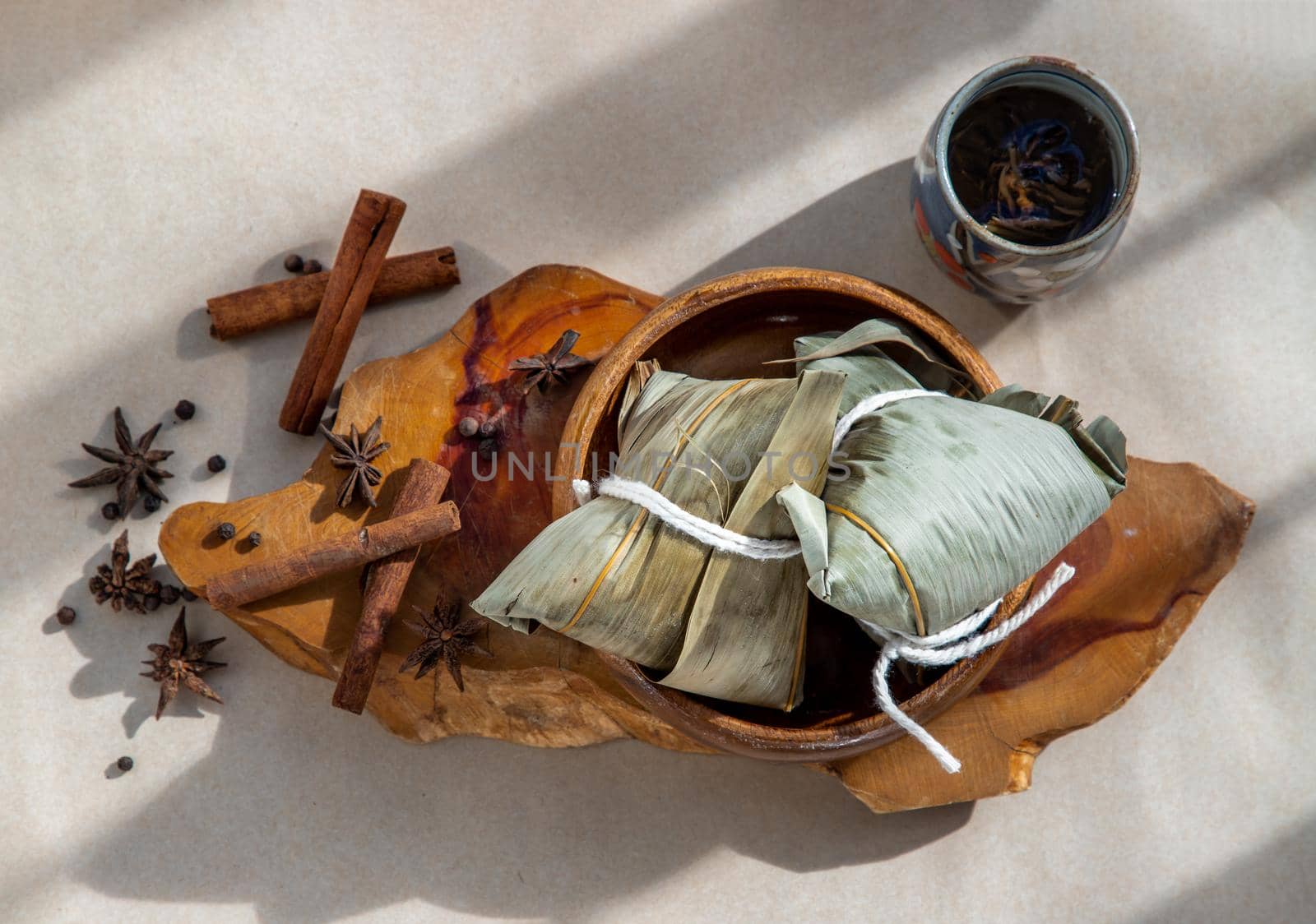 Chinese rice dumplings (Zongzi) shaped pyramidal wrapped by leaves ingredients on wooden plate. Famous asian tasty handmade food in dragon boat (duan wu) festival occasion.