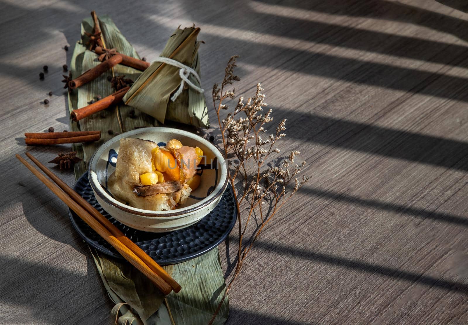 Chinese rice dumplings (Zongzi) shaped pyramidal wrapped by leaves ingredients on bowl chinese style and chopsticks. Famous asian tasty handmade food in dragon boat (duan wu) festival occasion.